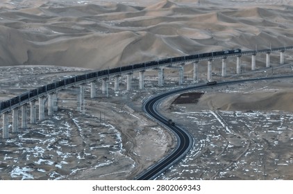 Freight train crosses elevated bridge over desert dunes and barren landscape. Aerial view of railroad infrastructure and transportation network through arid terrain.