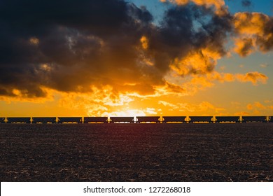 Freight Train Passing On On The Horizon Of Field  In The American Countryside. Sunset Light And The Stormy Sky Background. 