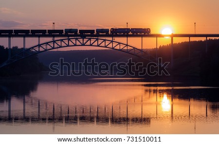 freight train rides on the railway bridge over the river during sunset, a summer evening the river Iset