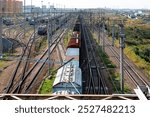 Freight trains on a busy railway junction with multiple tracks, switches, and overhead power lines, leading towards a distant city skyline and industrial area, representing transportation, logistics