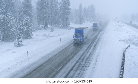 Freight trucks haul heavy cargo containers across the state of Washington and through a raging snowstorm. Cargo lorries navigate the slippery country road in low visibility during an intense blizzard.