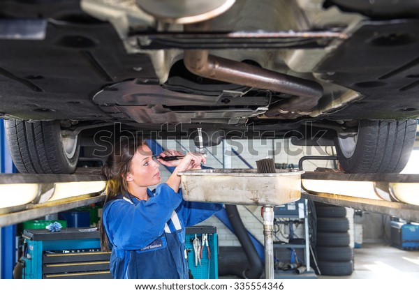 Fremale mechanic chaning the oil of a vehicle on\
a car lift, using a torque wrench to unscrew the oil tank. A\
collection vessel is placed underneath the outlet for environmental\
and recycling purposes