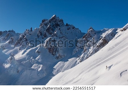 French Alps: Jagged mountain peak and steep ski piste against a blue sky
