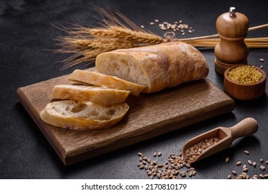 French baguette bread sliced on a wooden cutting board against a dark concrete background. Preparing the dinner table - Powered by Shutterstock