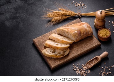 French baguette bread sliced on a wooden cutting board against a dark concrete background. Preparing the dinner table - Powered by Shutterstock