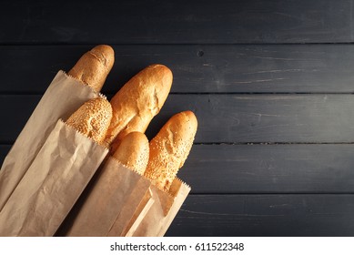 French baguettes with sesame seed in paper bags on black wooden background