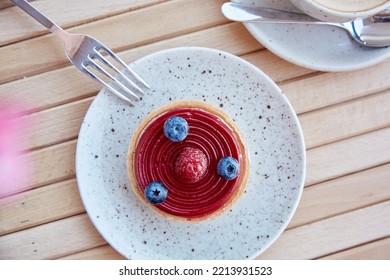 French Blueberry And Raspberry Tart On White Ceramic Plate With Cup Of Cappuccino. Coffee Time, Breakfast. Top View Food