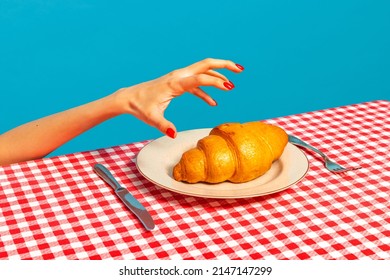French breakfast. Female hand tasting crispy croissant on plaid tablecloth isolated on bright blue background. Vintage, retro style interior. Complementary colors, Copy space for ad, text