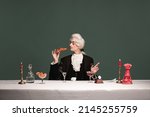 French breakfast. Portrait of young elegant man in peruke and vintage jacket sitting at table isolated on dark green background. Retro style, comparison of eras concept.