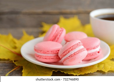 French Cakes Macaron Or Macaroon. Light Pink Macarons On A White Plate, A Cup Of Coffee, Yellow Leaves On A Vintage Wooden Background. Fall Snack Concept. Closeup