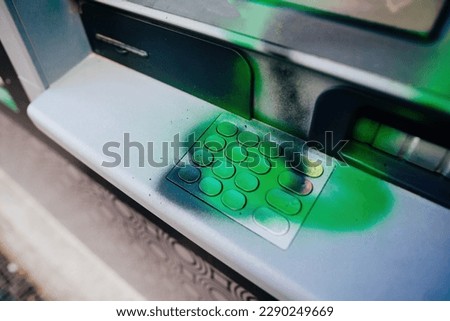 A French city ATM, damaged during a demonstration and covered in green paint graffiti. The keypad awaits removal so that the device could be used again by customers