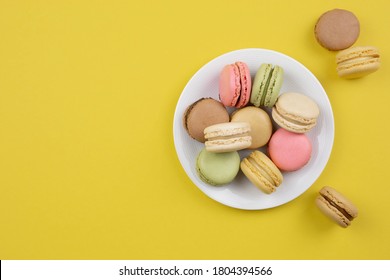 French colorful macaroons on a white plate. Yellow background. Top view. Copy space.