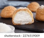 A French cream puff crack bun (Choux au Craquelin) in a plate, cut in a half filled with cream coconut filling topped with coconut grated. It