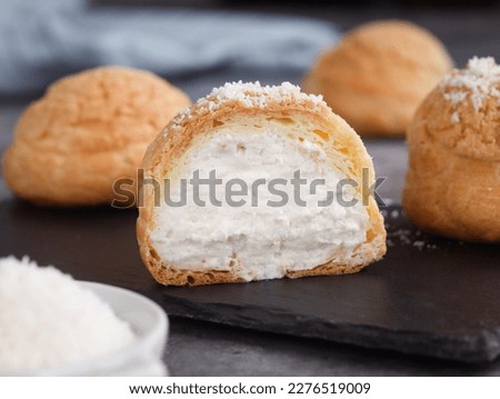 A French cream puff crack bun (Choux au Craquelin) in a plate, cut in a half filled with cream coconut filling topped with coconut grated. It's a dessert base of savory choux dough bun 
