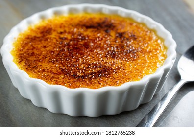 French Creme Brulee on the plate, with spoon on the side. On the marble table