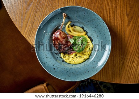 French cuisine - duck leg confit with polenta and caramelized pear, served in a blue plate on a wooden background. Restaurant food. View from above