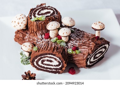 French dessert called Yule log or bûche de Noël with merengue mushrooms and mint leaves on top of chocolate glazing. Placed in front of Christmas tree. Decorated for Christmas Holidays or New year - Shutterstock ID 2094923014