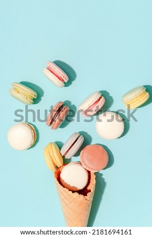 French dessert concept, Colorful pastel macarons are served in waffle cone on light blue background.