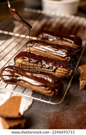 French dessert eclair, with dark chocolate glaze, chocolate glaze dripping from a spoon on eclairs.