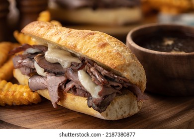 French dip sandwich and french fries with bowl of au jus in background on a wooden platter