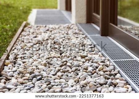 French drain with water Stones near House Wall Windows. Drainage system Stone Water Drains with Storm drain trench grating and Sewage around Building. 