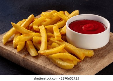 Patatas fritas francesas, tentempiés con ketchup, comida rápida sobre un fondo de piedra oscura, un plato lateral sobre una tabla de madera
