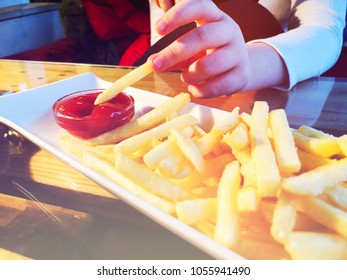 French Fries in the white plate with red cachup, girl hold one piece of french fries in her fingers
