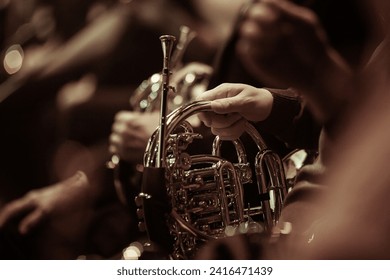 French horn in the hands of a musician in an orchestra close-up in dark colors
