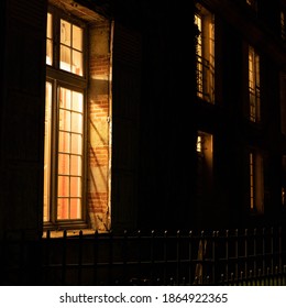 French House Lit From Inside. Dark Facade At Night And Brightly Lit Windows. Small Wooden Gate In Front Of The House. Stones And Exposed Bricks. An Autumn Night In France. Square Format