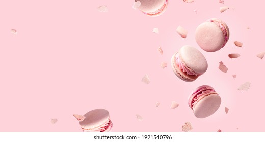 French macarons flying in the air among the crumbs on pink background. Levitation concept. Food wide banner with copyspace. - Shutterstock ID 1921540796