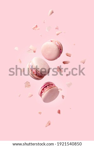 French macarons flying in the air among the crumbs on pink background. Levitation concept. food background. Pastel color. deconstruction food.