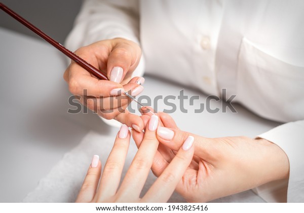 French manicure. Manicure\
master drawing white varnish on the nail tip with a thin brush,\
close up