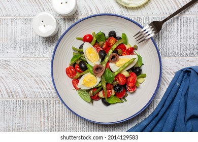 French Nicoise Salad With Anchovy, Green Beans, Tomatoes, Eggs, Black Olives, Capers On White Plate And White Wooden Background. Healthy Food, No Carb Diet Concept.