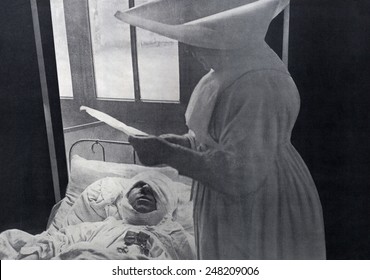 French nun attending a WW1 wounded soldier decorated in his hospital bed. 1916. He wears his two medals as well as a massive bandage for a head wound.