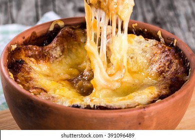 French Onion Gratin Soup In A Clay Pot, Authentic Recipe, Melted Gruyere Cheese On A Wooden Spoon, Close-up, Macro