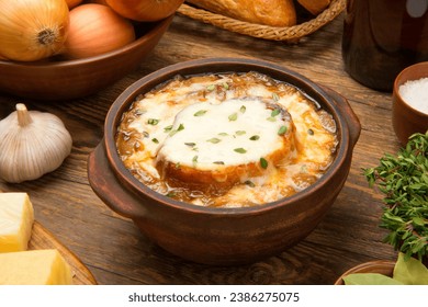 Sopa de cebolla francesa en un tazón de cerámica marrón sobre una mesa rústica de madera con ingredientes. 