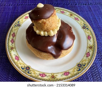 French Pastry: A Chocolate Nun Served On An Antique Dessert Plate Gilded With Fine Gold, Placed On A Blue Placemat.