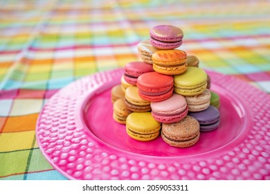 French pastry macarons tower presentation on pink dessert plate at bakery. Retro vintage checkered tablecloth table decor home kitchen. Assortment of pastel colored macaron of different flavors.