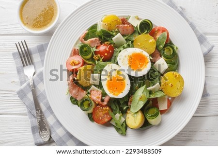 French peasant salad or salade paysanne with lettuce, bacon, cheese, tomatoes, potatoes and soft-boiled eggs closeup on the table. Horizontal top view from above
