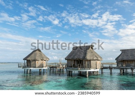 French Polynesia Tikehau atoll with pink coral reef lagoon and group of overwater bungalows under cloudy sky. Wideangle view.