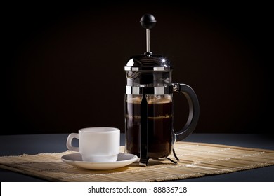 French Press Coffee Maker And Coffee Cup Studio Lit On Table With Dark Background