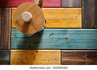 French Press Coffee Maker Made Of Wooden Material And Colorful Wooden Background And Caffe Standing On Wooden Table.