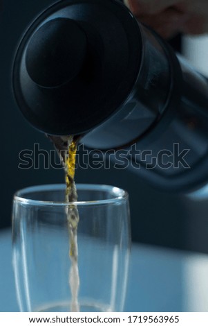 french press tea pouring into a glass with a double bottom on a white table and grey background 