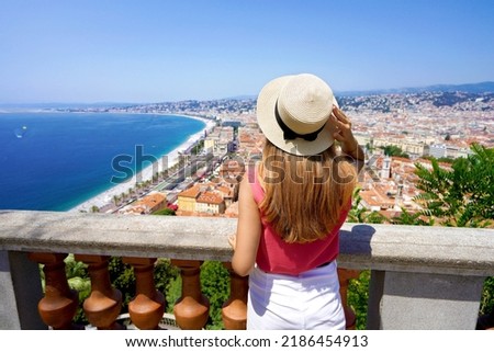 French Riviera. Back view of beautiful young woman holding hat enjoying the cityscape of Nice, France.