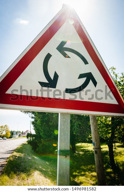 French road and new Roundabout\
sign indicating that a roundabout is ahead on the road sunlight\
flare