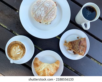 French Style Breakfast For Two In A Cafe. Latte Art Coffee With Freshly Baked Croissant On A Black Wooden Table, Piece Of Cake, Scones, And Egg And Bacon Roll. Directly Above. Healthy Food, Healthy Ea