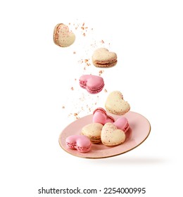 French sweet colorful heart shape cookies macarons macaroons with crumbs flying falling on vintage pink plate isolated on white background. Pastry shop card with copy space. Valentines day.