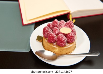 A French tartlet with raspberries and custard near open book on the table. Patisserie. Boulangerie. Epicure