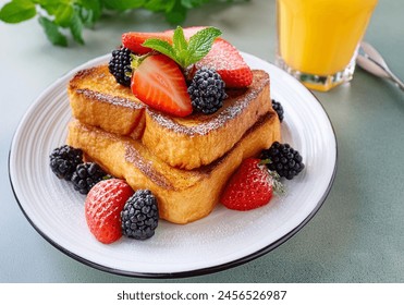 French toast crowned with vibrant strawberries, plump blackberries, and a fresh mint leaf, dusted delicately with powdered sugar accompained by a glass o orange juice.  - Powered by Shutterstock