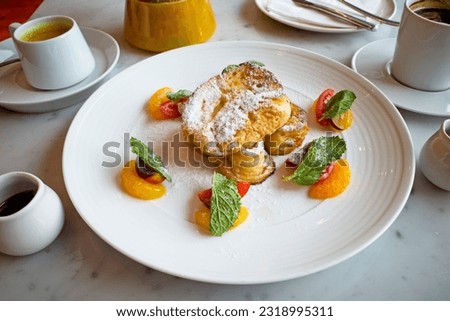 French toast with maple syrap, rasp berry sauce and fruits on a white plate.